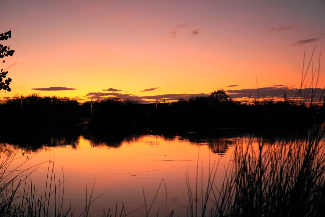 Jimmy Tonthat photo of lake at sunset. Rich reds and yellows and silhouetted hills 