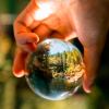 person holding glass ball with trees and water reflected on it